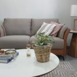 Detalhe da sala de atendimento, com sofá confortável, almofadas, mesa de centro, mesa lateral, abajur e objetos de decoração