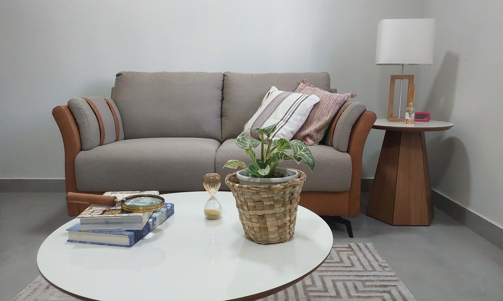 Detalhe da sala de atendimento, com sofá confortável, almofadas, mesa de centro, mesa lateral, abajur e objetos de decoração